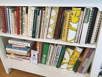 Photo of two shelves with multiple used cookbooks showing varied titles and binding types.