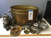 Photo showing full contents of the brass bin with assorted mixed metal items including pitchers, bowls, plates, flat irons, and a miniature metal object resembling a stove.