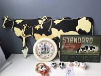 Overview showing 3 large wooden cow lawn stakes, round cow clock, painted wooden sign, salt and pepper shakers, and cow figurines arranged on table.