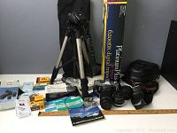 Photo showing Canon TX camera with FD 75-200mm zoom lens attached, plus 50mm and 28mm lenses, various filters, light meter, tripods, flash and accessories on a white table.