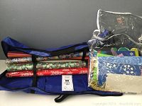Photo showing the blue zipper storage bag containing multiple wrapping paper rolls and a separate clear plastic bag filled with various gift bags.