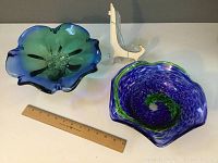 Photo showing two blue and green art glass bowls side by side with a wooden ruler for scale and white plastic easels behind.