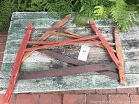 Pair of antique crosscut saws with wooden handles lying on a weathered green bench surrounded by bricks and ferns.