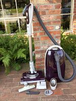 Full view of purple Sears Kenmore Progressive True HEPA canister vacuum cleaner with telescoping wand standing upright with several attachments arranged in front.