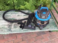 Full view of Vacmaster shop vac with hose and accessories on green bench outdoors