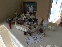 Full lot arranged on white table with visible pieces including ceramic rabbit figurine, bowl, and various miniatures in a basket.