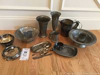 Overview of vintage pewter and silver plate items on hardwood floor including bowls, tankard, pitchers, vases, spoons, trays
