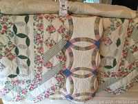 Photo showing three handmade quilts draped together in a row, highlighting patchwork floral and geometric designs with crocheted appliqué details.