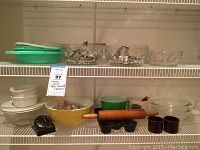 Wide view of kitchen shelf showing multiple items including glass bowls, cookie cutters, yellow Pyrex bowl, rolling pin, timer, and brown containers
