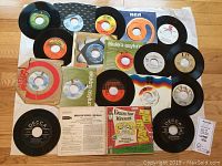 Overview photo of 18 vintage 45 RPM records, showing labels and some original sleeves including Capitol, RCA, Elektra/Asylum, Atlantic, and Decca