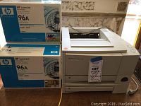 Photo showing HP LaserJet 2100TN printer next to two boxed HP 96A toner cartridges