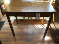 Full view of the rectangular wooden writing table with plywood top and straight legs, showing surface wear and single drawer in front.