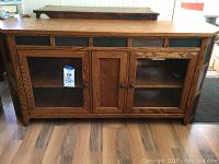 Full front view of oak veneer TV stand showing glass doors, solid doors, slate tile inserts, and wood knobs.