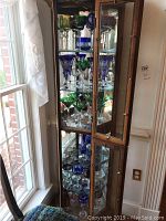Wooden display cabinet with multicolored crystal stemware across three shelves