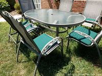 Outdoor view of green oval table with 6 chairs around it on grass.