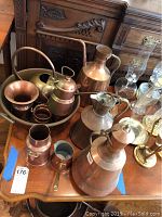 Image showing multiple copper items on a wood table including kettle, pitchers, basin, and glass oil lamps nearby.