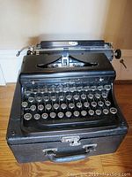 Front view of black Royal antique typewriter on its original carrying case showing round keys and top paper holder.