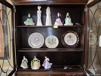 Front view of the display cabinet showing nine figurines and three decorative plates on three shelves.