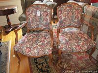 Frontal view of two armchairs with floral upholstery and wooden frames in a room.