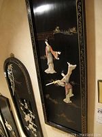 Close-up side view of one rectangular panel showing two traditional Asian figures in raised 2D form against black lacquer background