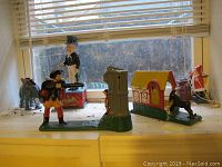 Five different metal banks displayed on a windowsill, including elephant, Uncle Sam, hunter, red house with dog, and a Christmas-themed Santa Claus bank.