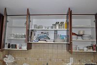 View of open kitchen cabinets showing multiple clear glass jar types, glass bowls, ceramic mugs, and folded fabric kitchen towels.