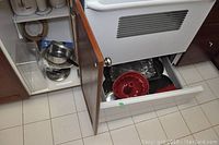 Kitchen cabinet with pots, pans, and kitchenware inside. Bottom drawer contains silicone bakeware and broiling tray.