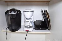 Front view of Keurig coffee maker, Braun coffee maker, and George Foreman grill on a shelf.