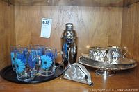 Four glass mugs with blue cornflower design on black tray with painted flower, metal drink mixer, small metal napkin holder, silver-plated cream and sugar set on tray with stand