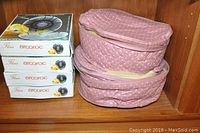 Four stacked boxes of Fleur Arcoroc dessert plates and two pink quilted fabric storage bags on a wooden shelf