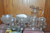 Four clear textured glass mugs and several bowls of varying sizes plus clear 8-inch glass jug against wood background.