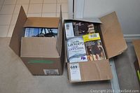 Two cardboard boxes filled with various books by named authors.