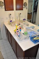 Bathroom counter full of assorted cleaning bottles, soap bars, and plastic baskets containing bathroom items
