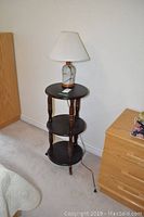 Three-tiered dark wood table in a corner, showing overall shape and condition with minor wear.