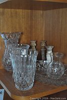 Shelf display showing three cut crystal vases, four marble candle holders, and part of crystal tray