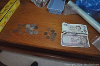 Overview of the assorted foreign coins and banknotes arranged on a wooden surface, showing complete banknotes and groupings of coins.