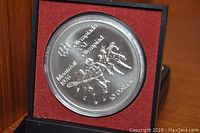Front side of the coin showing Olympic athletes and 10 dollar denomination in a display case