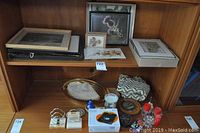 Shelf with framed and unframed botanical and landscape prints, leather photo albums, decorative tray, candles, answering system, and assorted small items