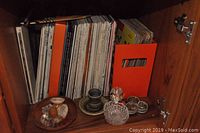 Vinyl records in sleeves stored in cabinet with some decorative items on surface including small bottles and a candle holder