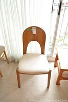Front and slightly angled views of a single heavy wood chair with an oval wooden backrest featuring a large central cutout and a beige upholstered seat.