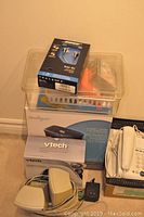Photo of stacked office electronics including Vtech cordless phone box, Bose headphones box on top, and plastic shredder.