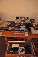 Photo of shelf with box containing assorted items including a metal bowl, wrapped napkins or placemats, and a barometer