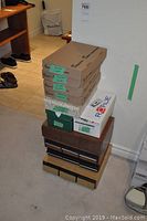 Stack of five large cardboard boxes, some labeled containing cassettes, two additional boxes including a white box marked 'Royce', and four cassette holders of wood and laminate appearance.