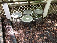 Four metal framed outdoor tables with round mosaic tops, each about 14 inches diameter, placed outdoors on leaf-covered ground.