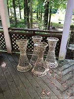 Four outdoor woven lattice flower pot stands arranged closely on a porch deck providing a front perspective showing the height and shape.