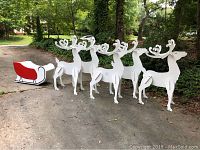 Group of five white wooden reindeer and one red-and-white wooden sleigh arranged on driveway