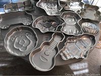 Photo showing multiple aluminum cake pans with various shaped designs including a guitar, lion, gingerbread man, dog, and clown.