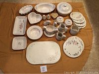 Full overview of all Pfaltzgraff Rose serving pieces and placemats arranged on fabric.