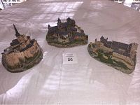 Photo showing three castle models placed on a table covered with plastic, including Alcazar, Mont Saint Michel, and Braunfels Castle. Each miniature castle is finely detailed with textured walls and roofs.