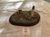 Front angle view of detailed Boston Light diorama with lighthouse and buildings on rocky base on oval wooden stand.